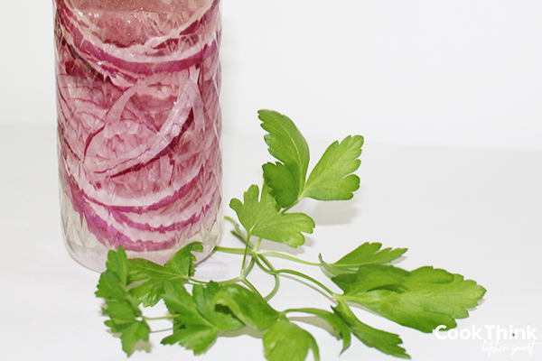 marinated red onions in a clear glass jar, with a sprig of parsley
