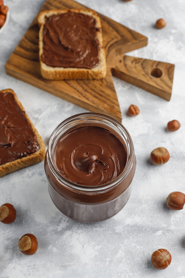 Chocolate spread or nougat cream with hazelnuts in glass jar on