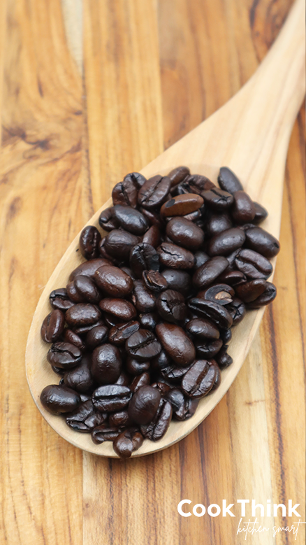 whole coffee beans on wooden spoon